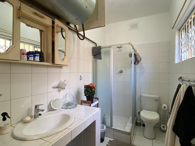 A functional bathroom featuring a shower enclosure, toilet, and vanity basin, with tiled finishes and visible plumbing infrastructure requiring cosmetic updates.