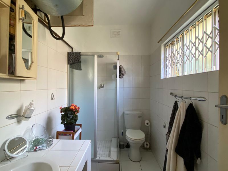 A functional bathroom featuring a shower enclosure, toilet, and tiled vanity. The space requires cosmetic updates to improve its dated appearance.