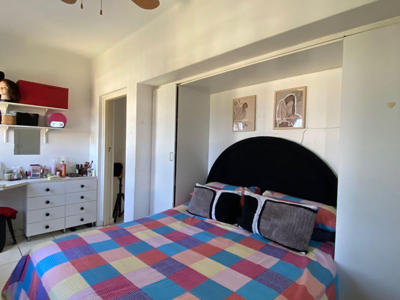 A bedroom featuring a built-in wardrobe and a ceiling fan, offering a functional layout with neutral wall finishes.