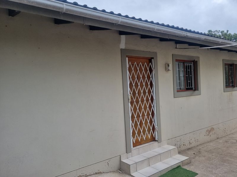 Exterior view of the apartment rear facade featuring a timber door with security gate, tiled steps, and window security bars.