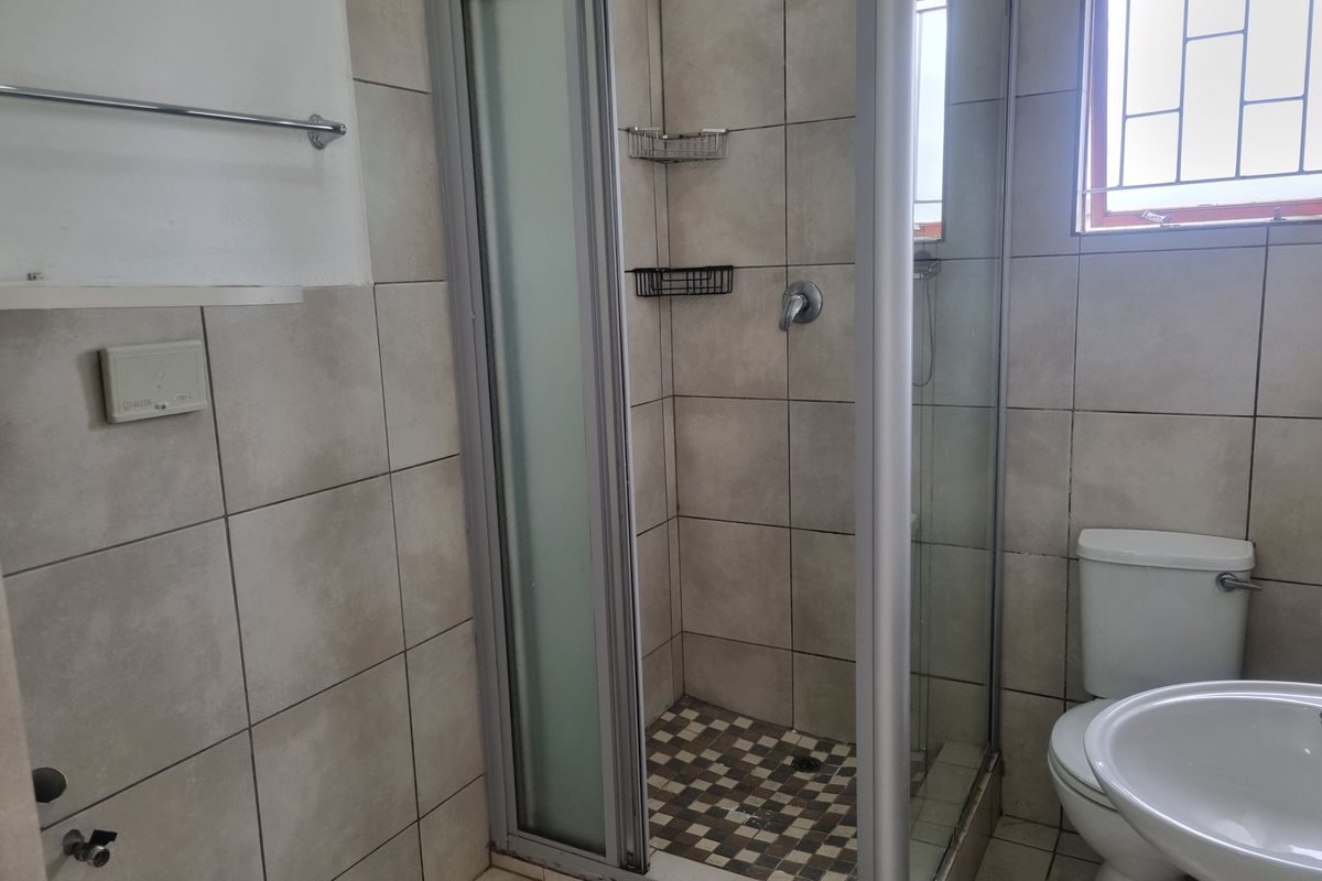 A functional bathroom featuring a shower enclosure, pedestal basin, and toilet, finished with neutral ceramic wall and floor tiles.