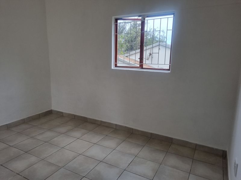 An empty bedroom featuring neutral tiled flooring and a window fitted with security bars, offering a clean and blank canvas for personalization.