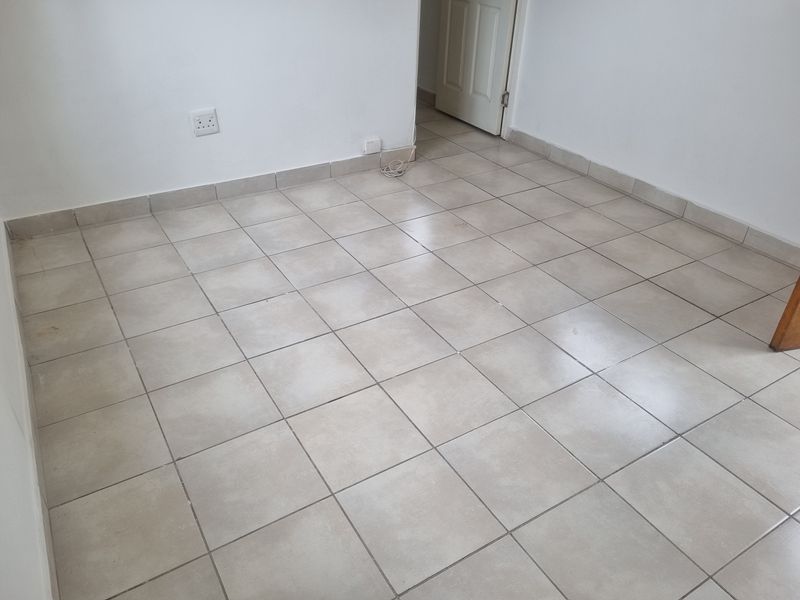 An empty bedroom featuring neutral ceramic floor tiles, white walls, and standard electrical fixtures, providing a blank canvas for interior design.