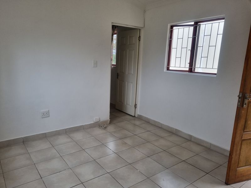 An empty bedroom featuring tiled flooring, white walls, and a window fitted with security bars.