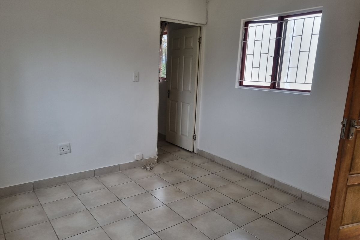 An empty bedroom featuring tiled flooring, white walls, and a window fitted with security bars.