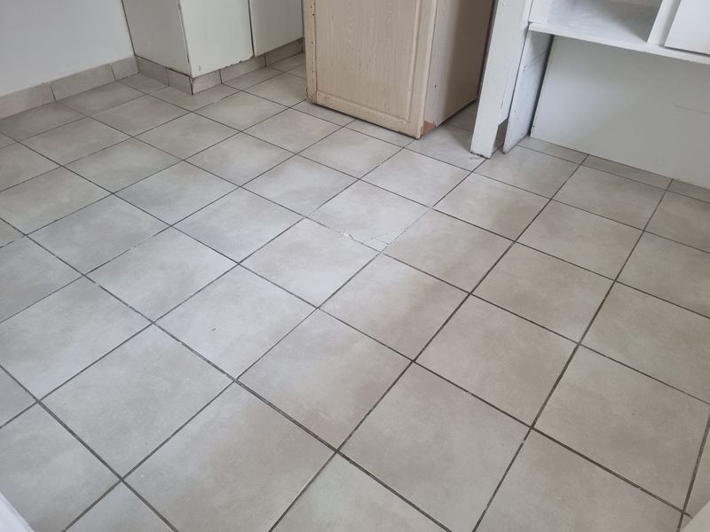 An empty kitchen area featuring light-colored floor tiles and basic built-in cabinetry, showing signs of wear and a cracked floor tile.