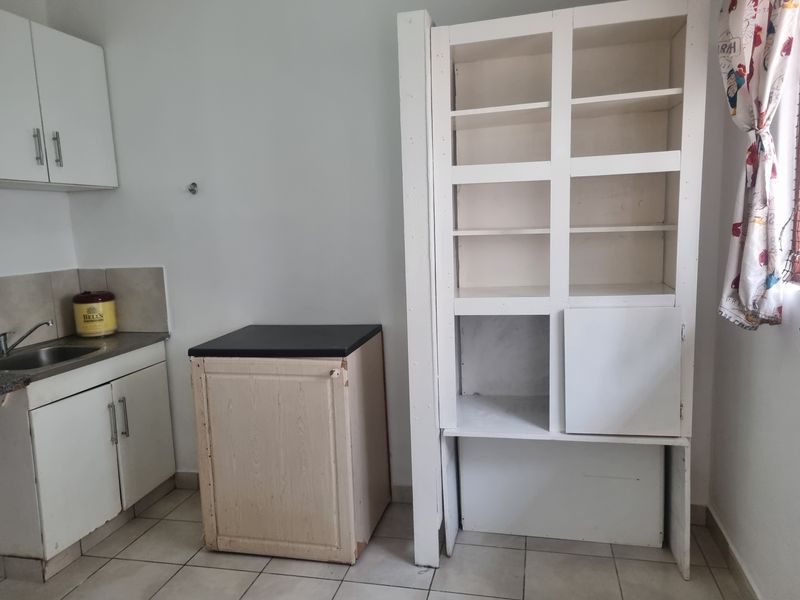 A functional kitchen area featuring basic cabinetry, a stainless steel sink, and built-in shelving, with tiled flooring throughout.