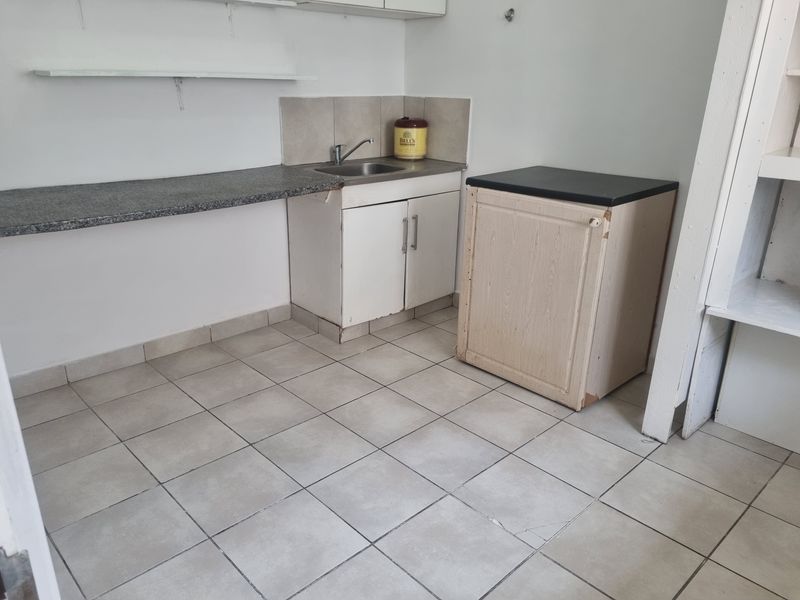 A compact kitchen area featuring tiled flooring, a stainless steel sink, granite countertop, and built-in cabinetry, offering a functional space ready for modernization.