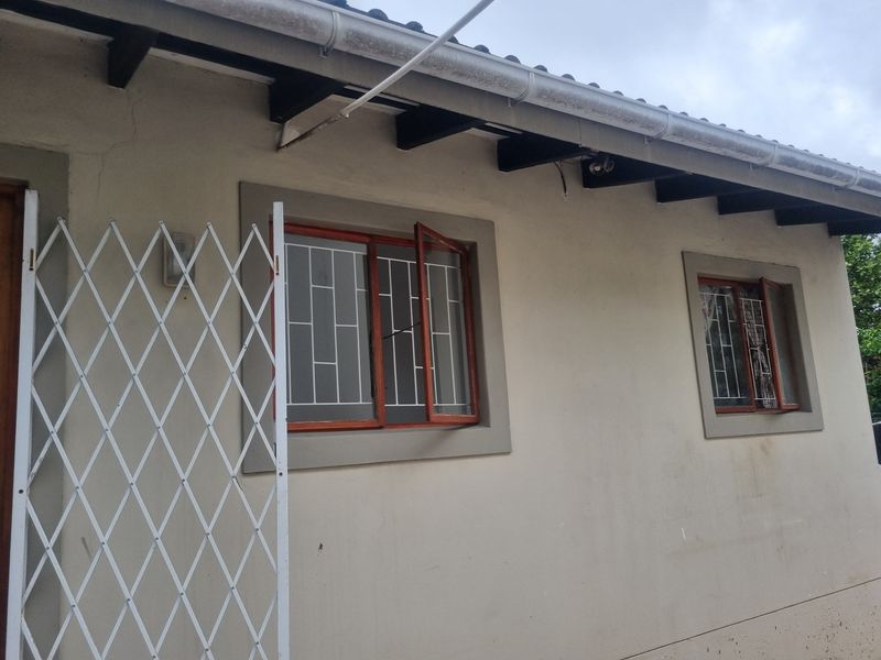 Exterior view of the property featuring timber window frames with security bars, exposed rafters, and guttering along the roofline.