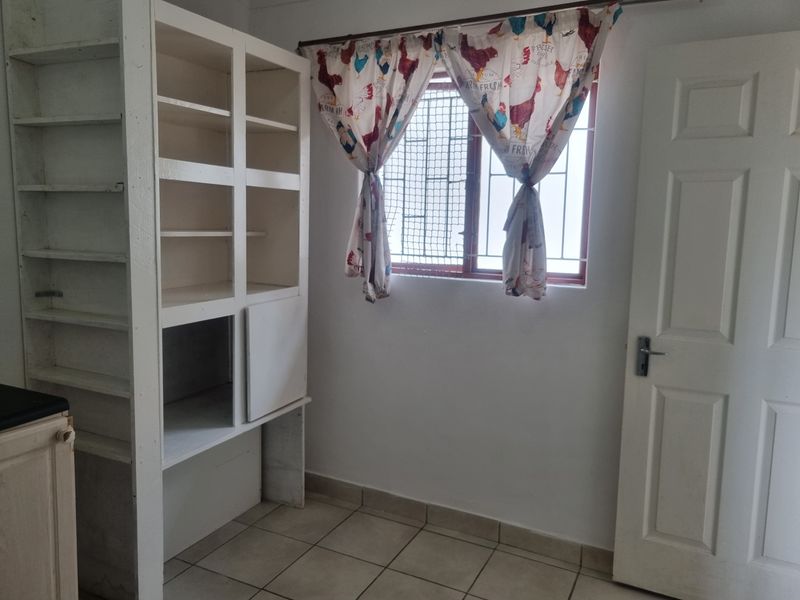 A functional scullery or utility area featuring built-in open shelving, tiled flooring, and a window with security bars.