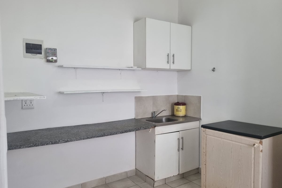 A compact kitchen area featuring granite countertops, a stainless steel sink, built-in cabinetry, and tiled flooring, offering a functional space ready for updates.