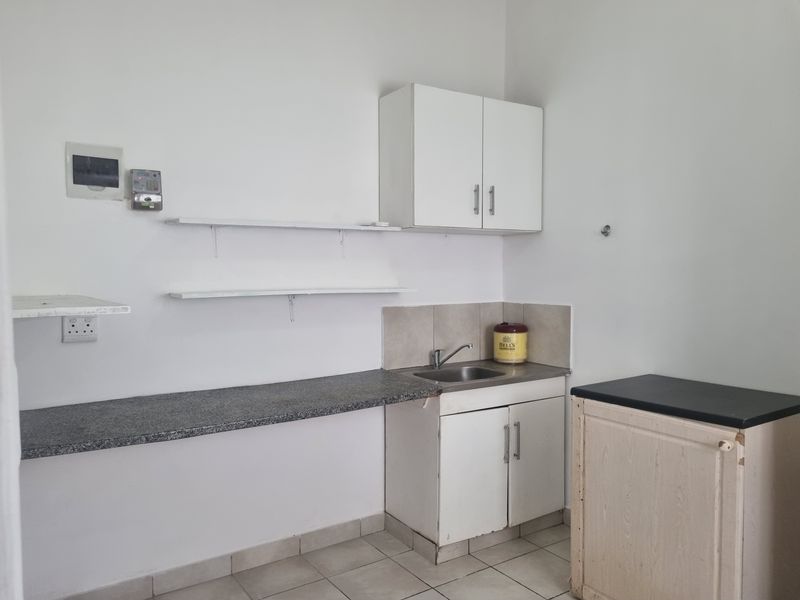 A compact kitchen area featuring granite countertops, a stainless steel sink, built-in cabinetry, and tiled flooring, offering a functional space ready for updates.