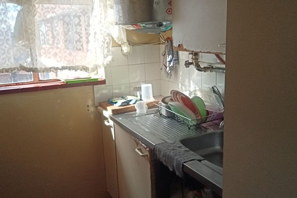 A compact kitchen area featuring a stainless steel sink, tiled splashback, and wall-mounted water heater, requiring significant renovation and modernization.
