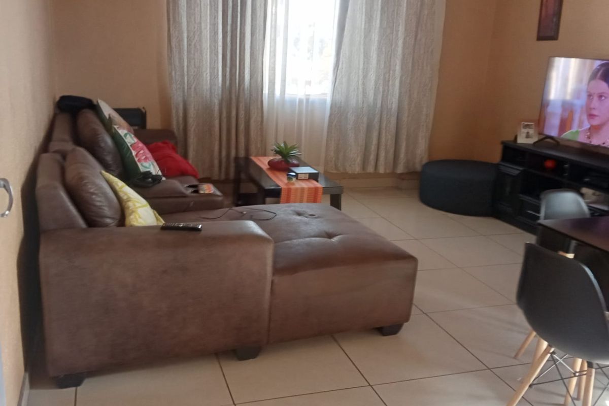 A comfortable living room featuring tiled flooring and large windows with curtains, providing a functional and well-lit space for relaxation.