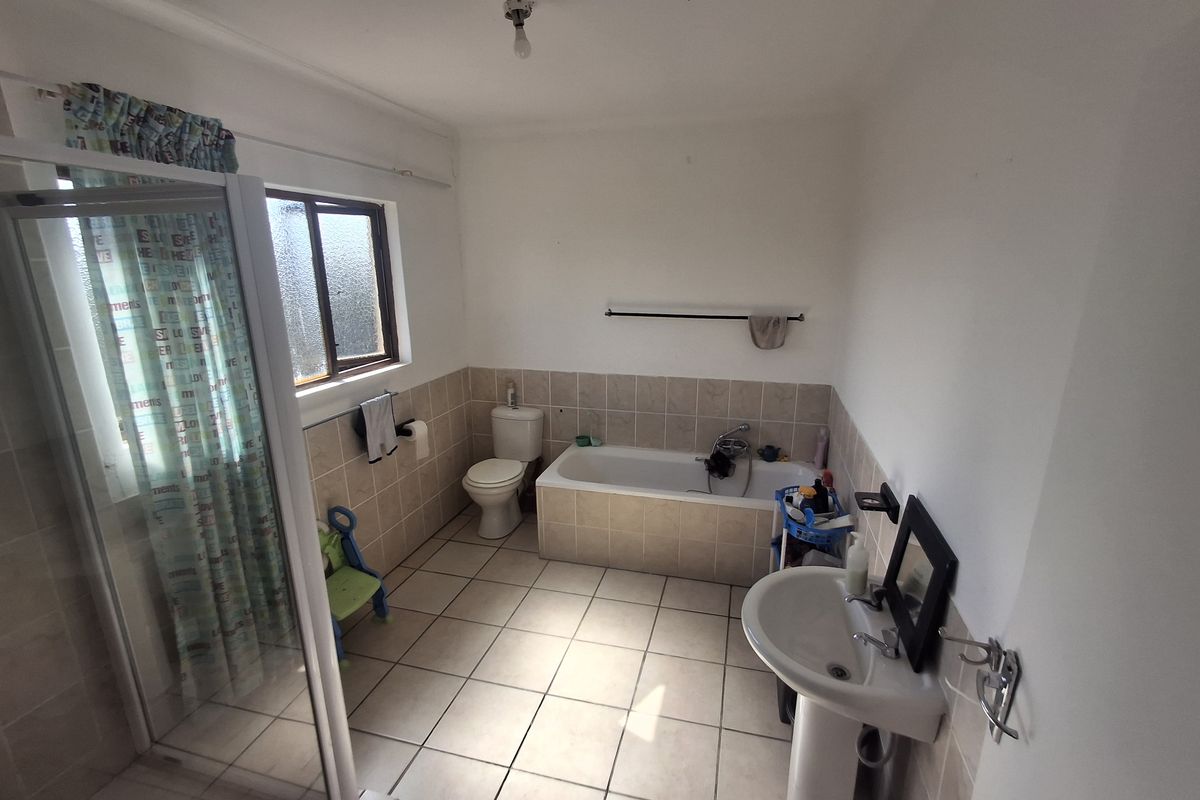 A functional bathroom featuring a tiled bathtub, separate shower enclosure, pedestal basin, and toilet with neutral wall and floor tiling.