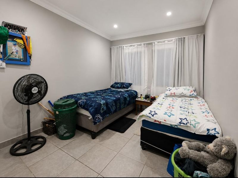 A functional bedroom featuring tiled flooring and recessed downlighting, currently configured with two single beds and window treatments.