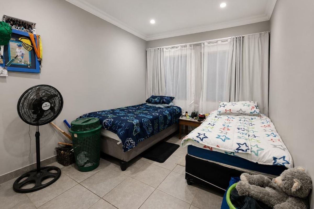 A functional bedroom featuring tiled flooring and recessed downlighting, currently configured with two single beds and window treatments.