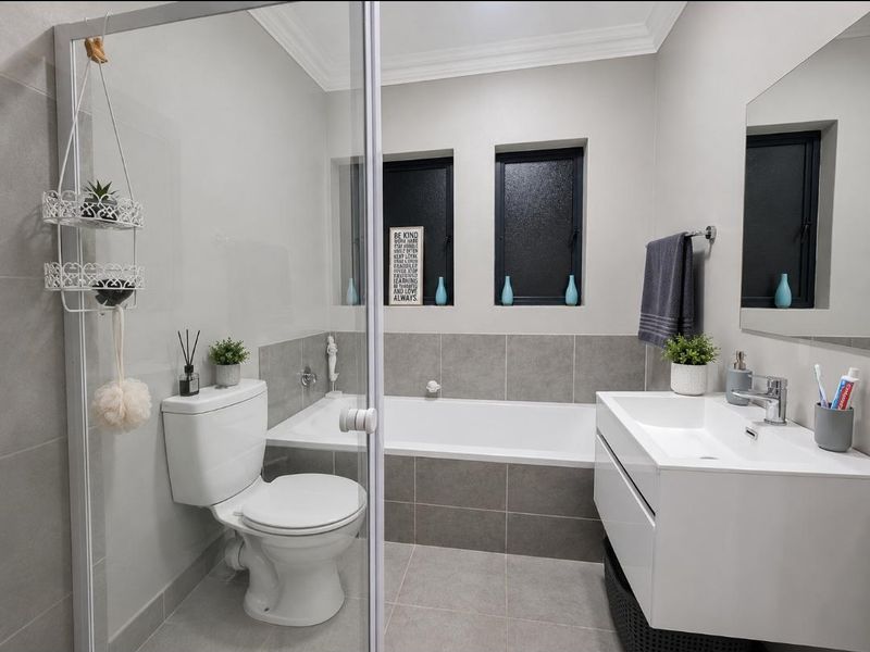 A modern, well-maintained bathroom featuring a built-in bathtub, wall-mounted vanity, and a glass-enclosed shower area with neutral grey tiling.