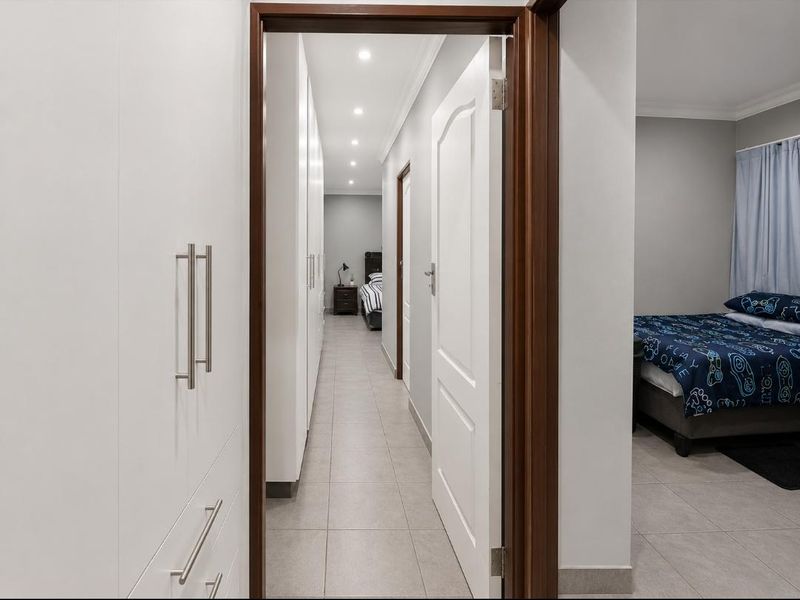 A well-lit hallway featuring extensive built-in cabinetry, neutral tiled flooring, and recessed downlighting, providing seamless access between rooms.