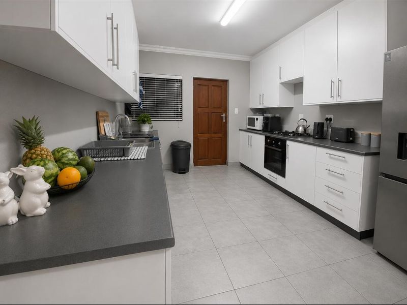 A well-maintained galley-style kitchen featuring white cabinetry, dark countertops, built-in oven, gas hob, and neutral tiled flooring.
