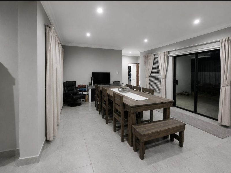 Spacious dining area featuring neutral tiled flooring, recessed downlighting, and large sliding glass doors providing access to the outdoor area.