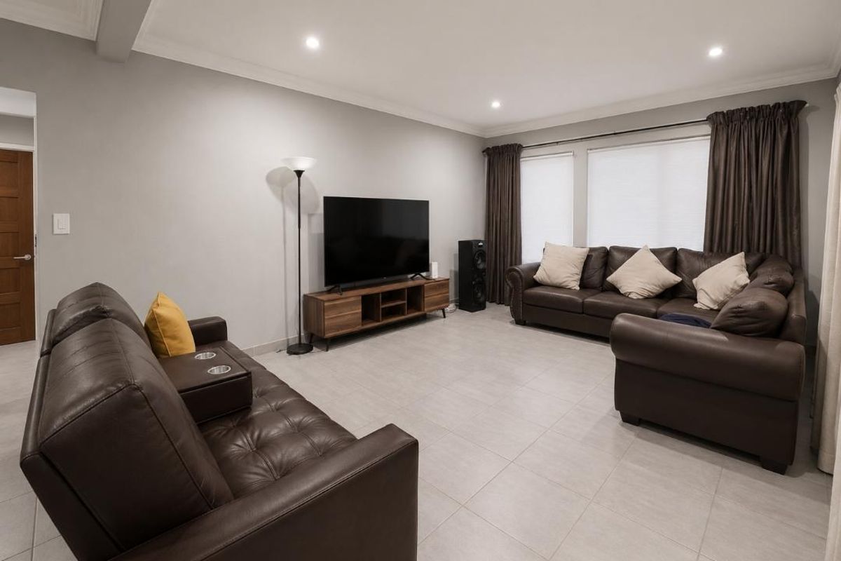 A spacious living room featuring neutral tiled flooring, recessed downlighting, and decorative cove cornicing, providing a comfortable and well-maintained living area.