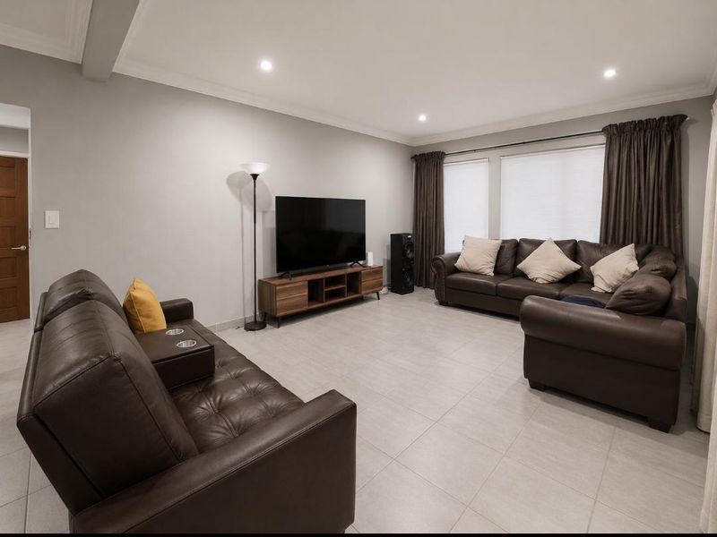 A spacious living room featuring neutral tiled flooring, recessed downlighting, and decorative cove cornicing, providing a comfortable and well-maintained living area.