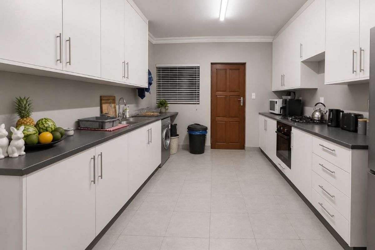 A well-maintained galley-style kitchen featuring white cabinetry, dark countertops, built-in oven, gas hob, and tiled flooring with a functional layout.