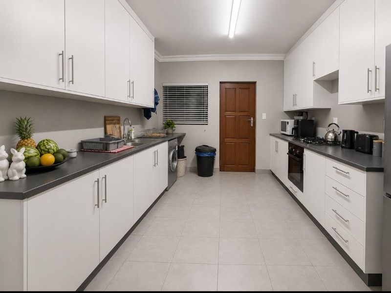 A well-maintained galley-style kitchen featuring white cabinetry, dark countertops, built-in oven, gas hob, and tiled flooring with a functional layout.