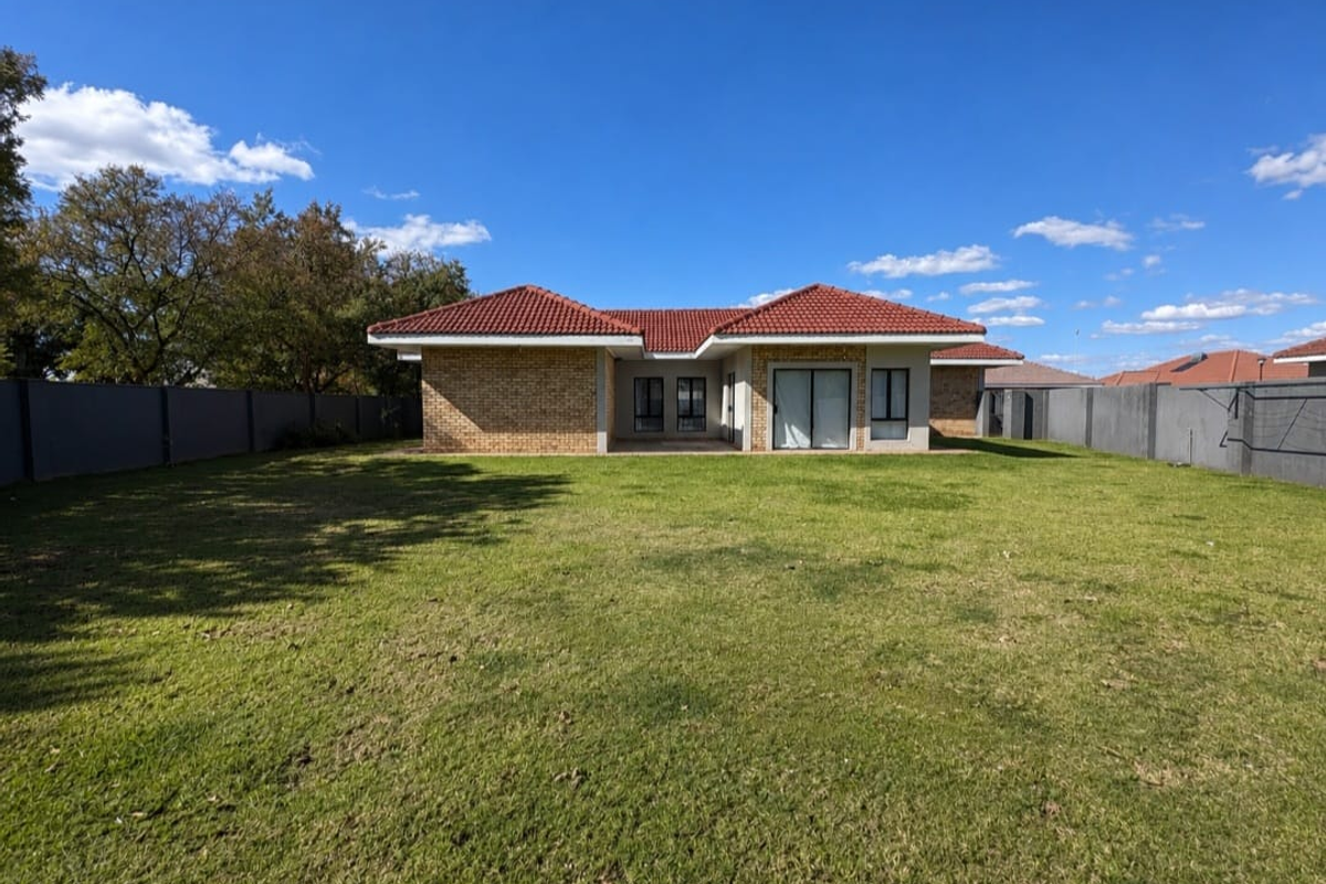 A view of the rear elevation of the property featuring a brick facade, tiled roof, sliding glass doors, and a spacious private lawn.