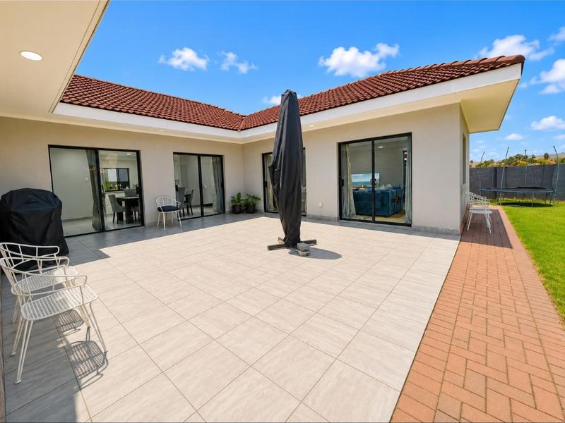 Spacious tiled patio area featuring multiple sliding glass door access points, recessed lighting, and an adjoining brick-paved walkway leading to the garden.