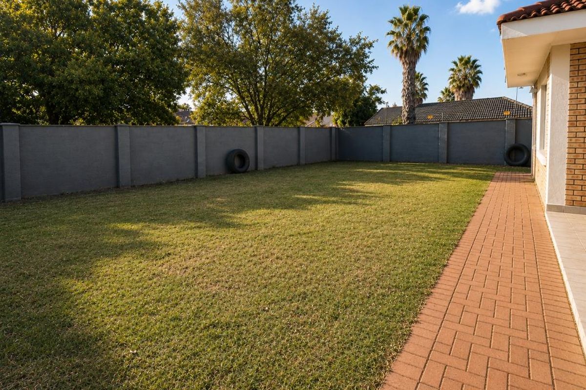 A private rear garden featuring a well-maintained lawn, perimeter boundary wall, and a paved walkway leading along the side of the townhouse.