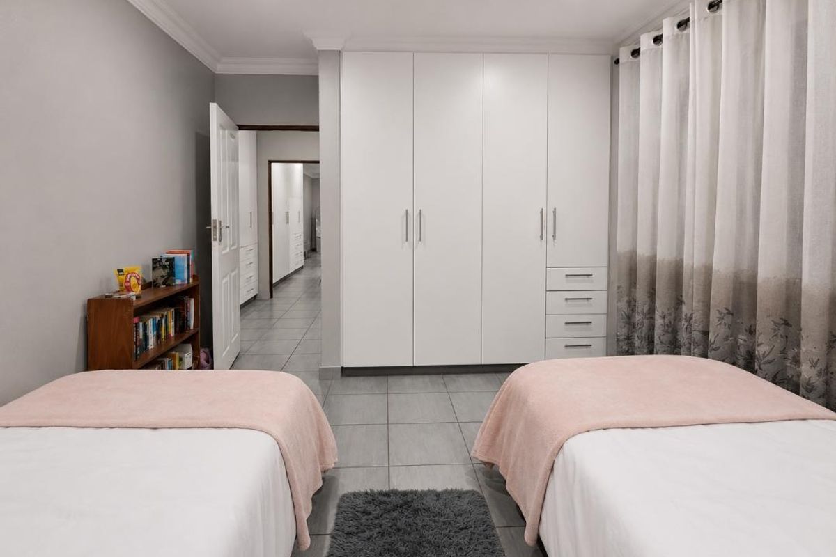 A well-maintained bedroom featuring neutral tiled flooring, recessed downlighting, and ample built-in cupboard storage.