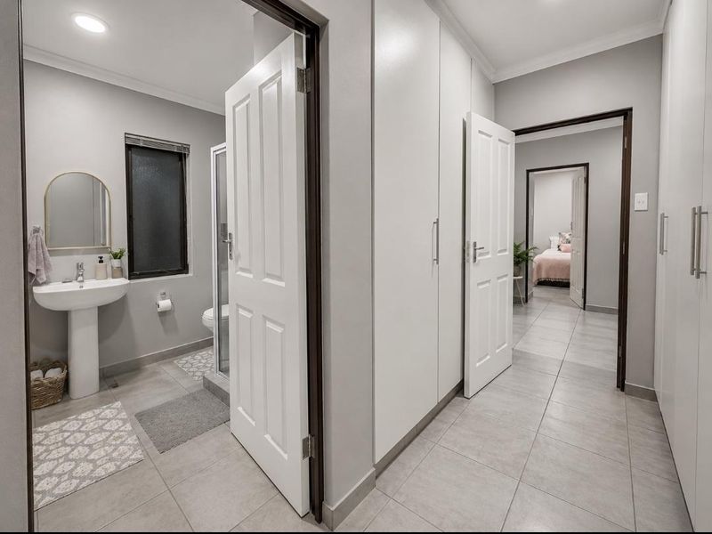 A bright, modern hallway featuring extensive built-in storage cupboards, tiled flooring, and direct access to an adjacent bathroom and bedroom.