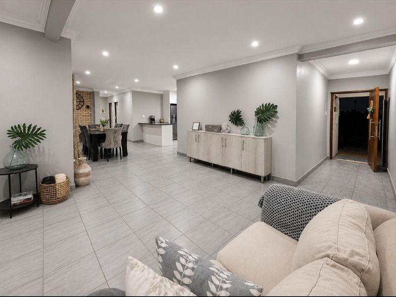 Spacious open-plan living and dining area featuring neutral tiled flooring, recessed downlighting, and a modern kitchen island with integrated cabinetry.