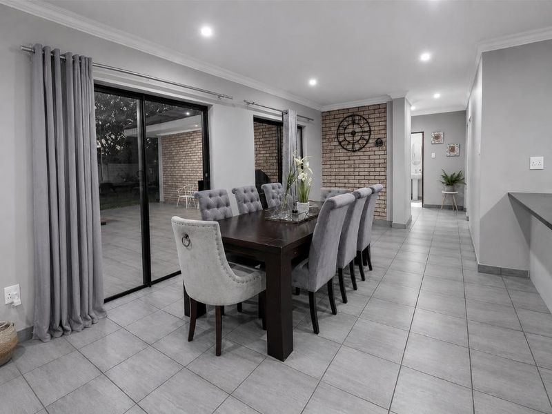 Spacious dining area featuring tiled floors, recessed lighting, and a striking exposed brick feature wall with direct access to the outdoor patio.