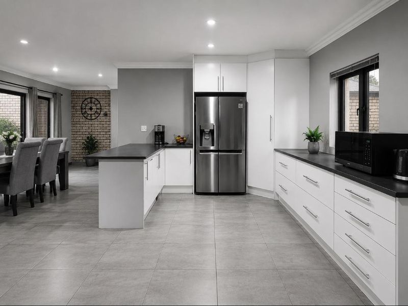 Modern open-plan kitchen and dining area featuring sleek white cabinetry, dark countertops, tiled floors, and a stylish exposed brick feature wall.