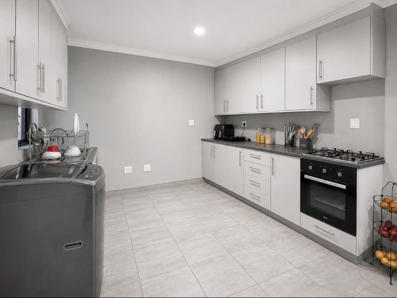 Modern kitchen featuring light grey cabinetry, dark countertops, a gas hob, built-in oven, and tiled flooring in a clean, functional layout.