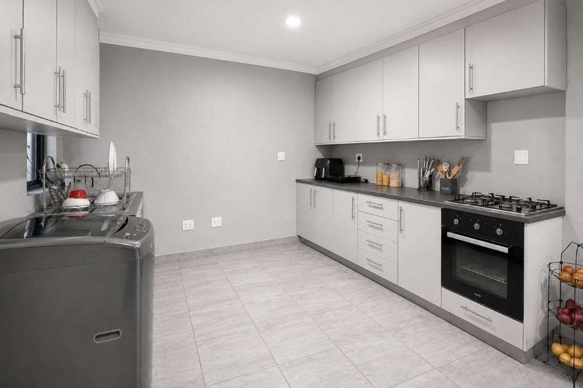 Modern kitchen featuring light grey cabinetry, dark countertops, a gas hob, built-in oven, and tiled flooring in a clean, functional layout.