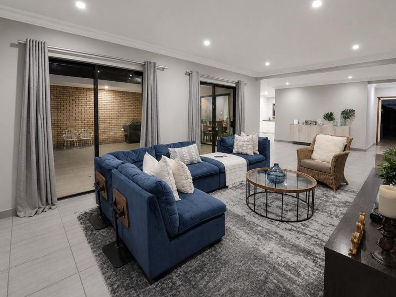 Spacious open-plan living area featuring neutral tiled flooring, recessed downlighting, and large sliding glass doors providing seamless access to the outdoor patio.