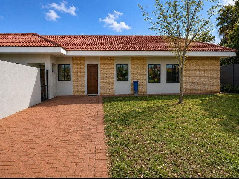 Front view of a townhouse featuring a terracotta tiled roof, brick and plaster facade, paved driveway, and a well-maintained front lawn.