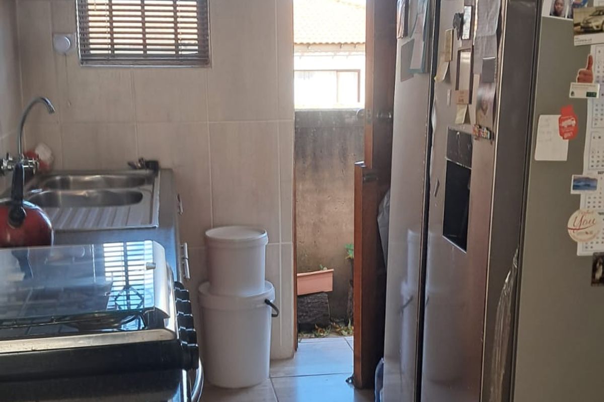 A compact kitchen featuring tiled walls, dark countertops, a built-in extractor fan, and direct access to an outdoor area.