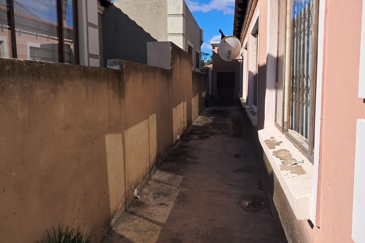 A narrow side passage of the property featuring a concrete walkway, boundary wall, and exterior window access with security bars.