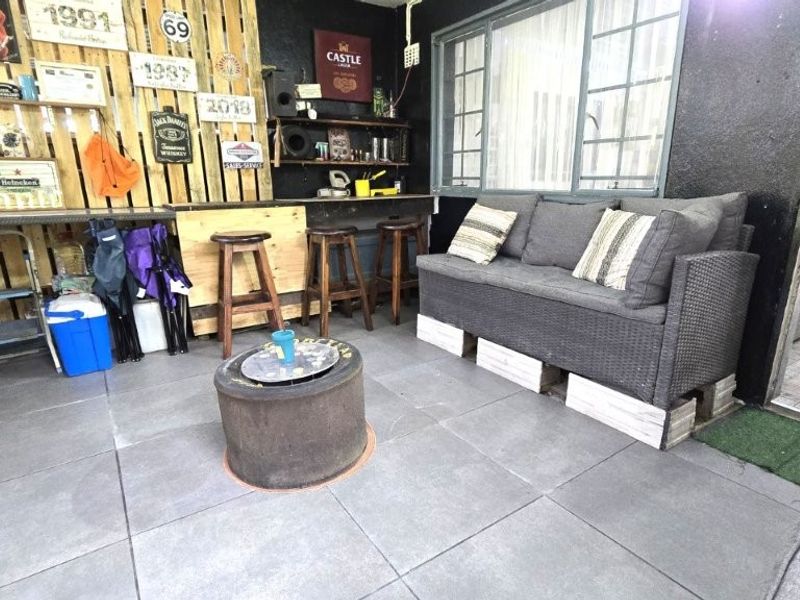 Covered patio area featuring tiled flooring, a built-in bar counter, and security-barred windows, offering a functional outdoor entertainment space.