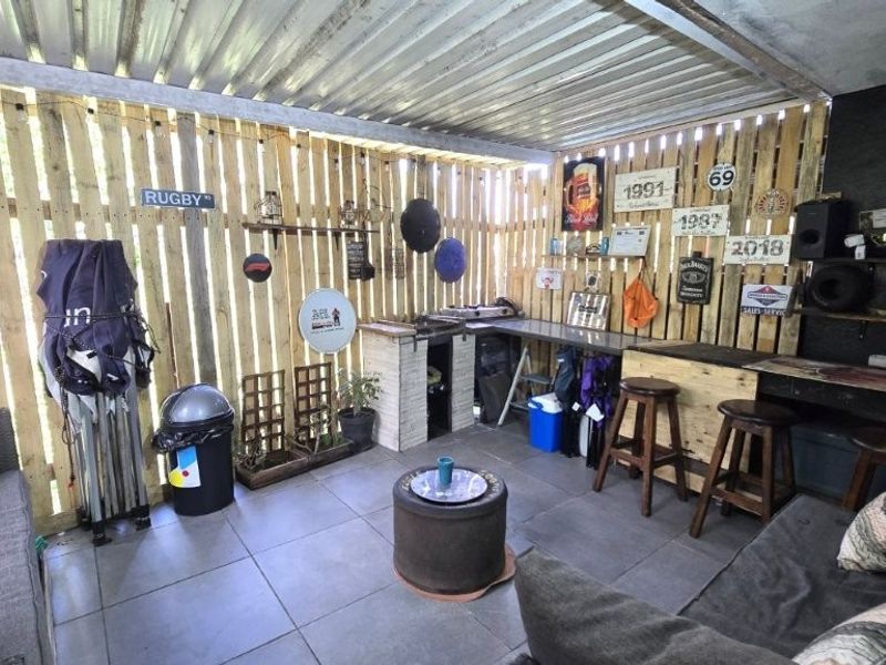 A covered outdoor patio area featuring timber pallet wall cladding, tiled flooring, and a built-in bar counter, suitable for casual outdoor entertaining.