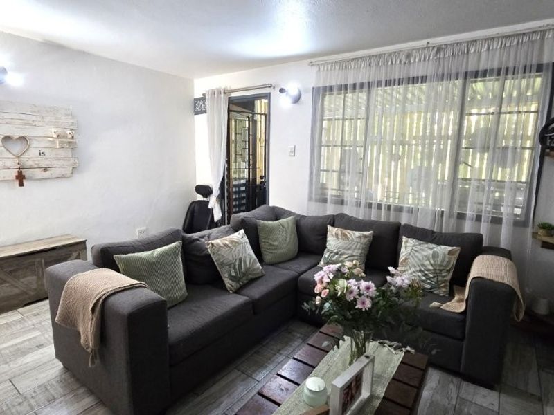 A comfortable living room featuring tiled flooring, wall-mounted lighting, and direct access to an outdoor area through a security gate.