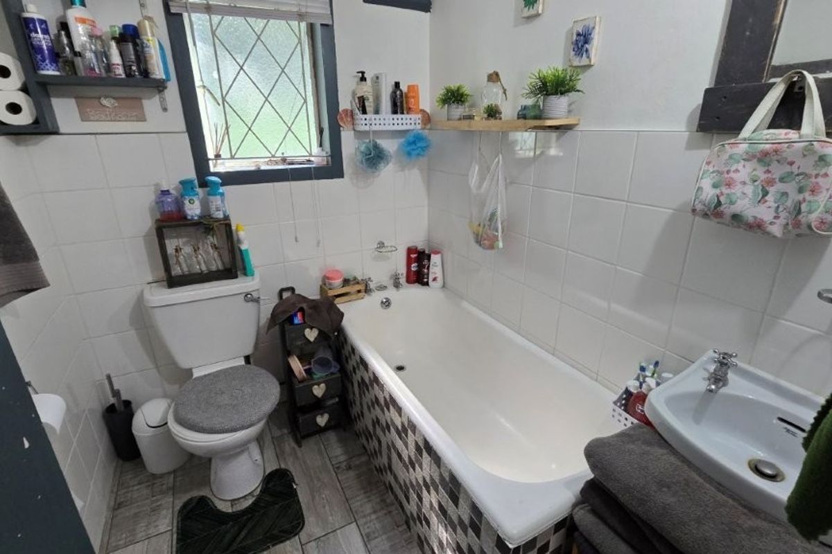 A compact bathroom featuring a bathtub, pedestal basin, and toilet with white wall tiling and patterned floor tiles.