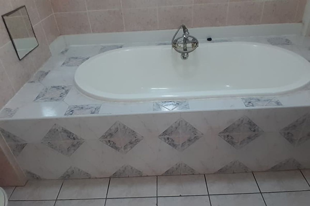 A bathroom featuring a built-in bathtub with decorative tiled surround, ceramic floor tiles, and wall-mounted fixtures.