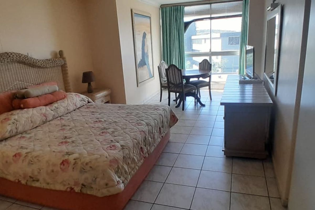 A spacious bedroom featuring tiled flooring, built-in cupboards, and large windows providing natural light and access to an outdoor area.