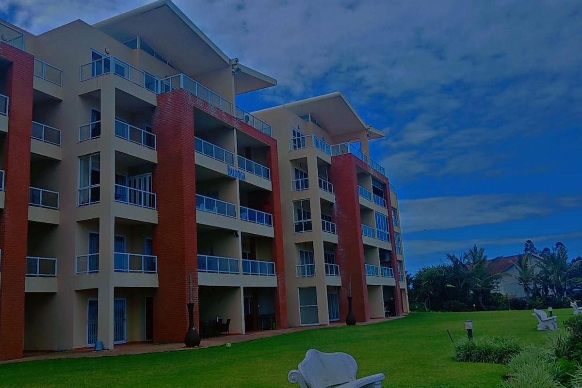 A multi-story apartment building featuring brick and plaster facade, private balconies with glass railings, and well-maintained surrounding lawn areas.